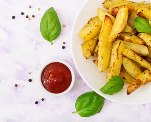 Piatto di patate, ciotola con ketchup e foglie di basilico