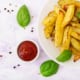 Piatto di patate, ciotola con ketchup e foglie di basilico