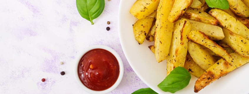 Piatto di patate, ciotola con ketchup e foglie di basilico