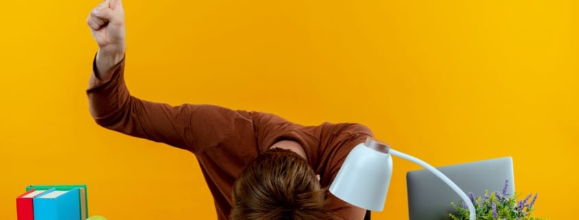 persona affranta alla scrivania con la testa appoggiata sul tavolo e una mano alzata